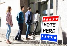 People entering building with "Vote Here" sign nearby.