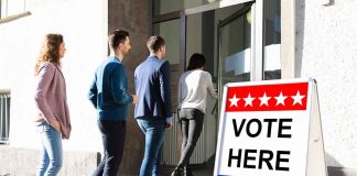 People entering building with "Vote Here" sign nearby.