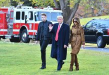 Three people walking on grass near fire truck.