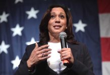 Woman speaking with microphone, American flag background.