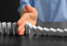 Hand stopping falling row of dominoes