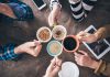 Hands holding different mugs over table.