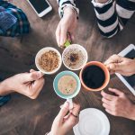 Hands holding different mugs over table.