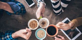 Hands holding different mugs over table.