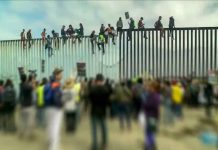 People sitting on high metal fence during protest.