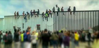 People sitting on high metal fence during protest.