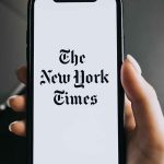 Hand holding phone with New York Times logo.