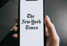 Hand holding phone with New York Times logo.