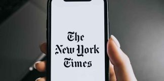 Hand holding phone with New York Times logo.