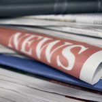 Stack of newspapers with news headline visible.