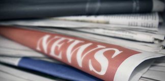 Stack of newspapers with news headline visible.