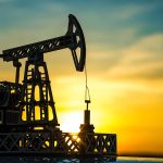 Oil pump jack silhouetted against sunset sky.