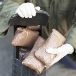 Person handling packages wearing gloves and green jacket