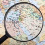 Magnifying glass over Middle East map highlighting Israel and Egypt.