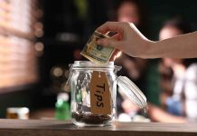 Hand placing dollar bill into a tip jar.