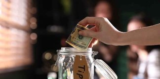 Hand placing dollar bill into a tip jar.