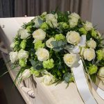 White roses on a coffin with ribbon.