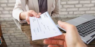 Hands exchanging a check near a laptop.