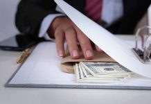 Hand concealing cash under a folder on a desk.