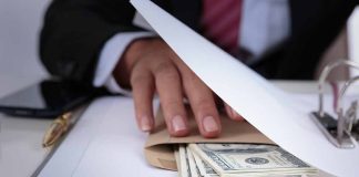 Hand concealing cash under a folder on a desk.