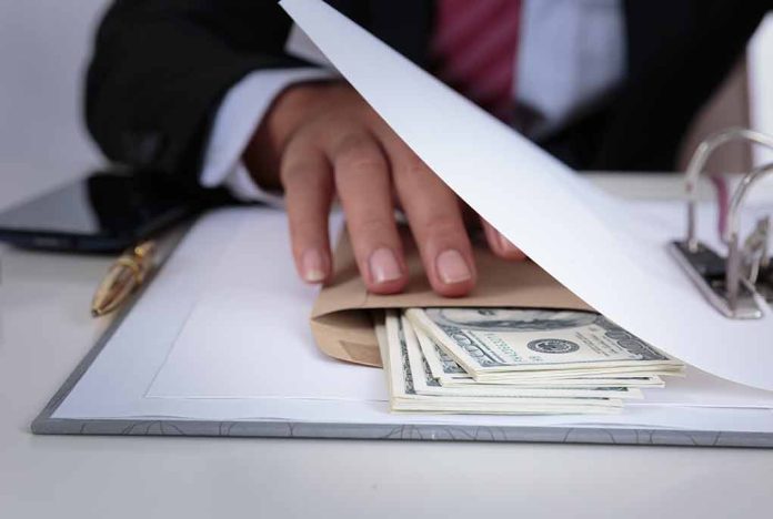 Hand concealing cash under a folder on a desk.