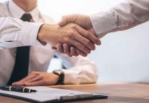 Two people shaking hands over a desk.