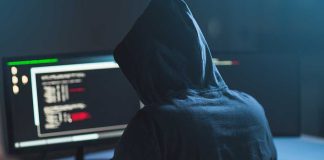 Person in hoodie coding on computer screens.