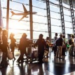 Passengers waiting at airport gate with airplane outside window.