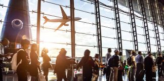 Passengers waiting at airport gate with airplane outside window.