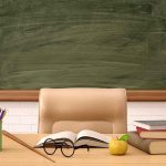 Classroom desk with books, apple, and chalkboard