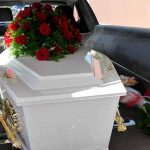 White coffin with red roses inside a hearse