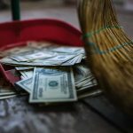 Broom sweeping dollar bills into red dustpan floor