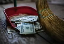 Broom sweeping dollar bills into red dustpan floor