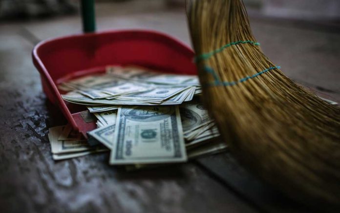 Broom sweeping dollar bills into red dustpan floor