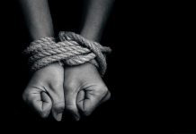 Hands bound with rope against a dark background.