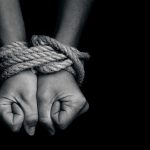 Hands bound with rope against a dark background