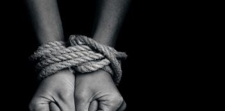 Hands bound with rope against a dark background