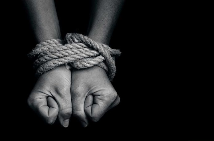 Hands bound with rope against a dark background