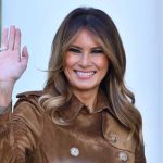 Person smiling and waving wearing a brown coat