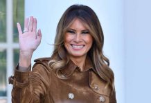 Person smiling and waving wearing a brown coat