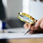 Person examining document with magnifying glass.