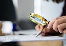 Person examining document with magnifying glass.