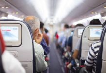 Passengers seated in airplane cabin with screens visible