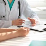 Doctor consulting patient with clipboard and pen.