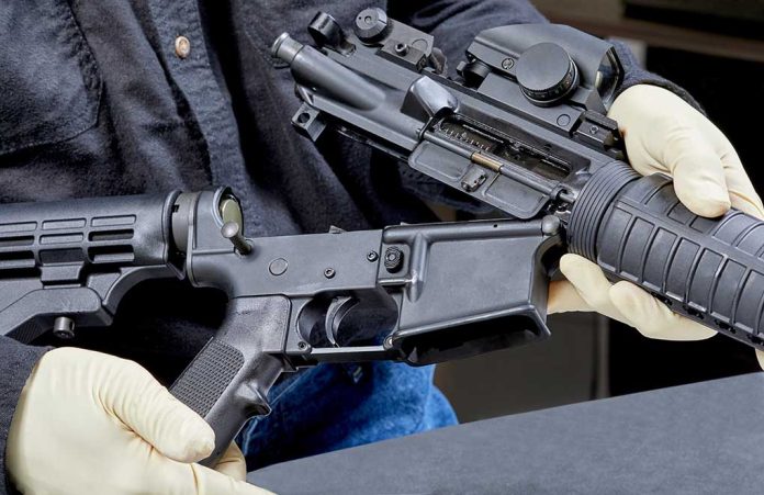 Person assembling a rifle with gloved hands.