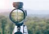 Rifle scope aiming at a distant tree.