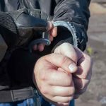 Gloved officer handcuffing a person's hands outdoors