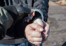 Gloved officer handcuffing a person's hands outdoors