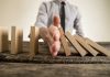 Hand stops falling dominoes on wooden table