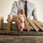 Hand stops falling dominoes on wooden table